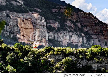 Rescue helicopter in the Montserrat massif, a mountain in the province of Barcelona, on a day with blue sky and white clouds 125398252