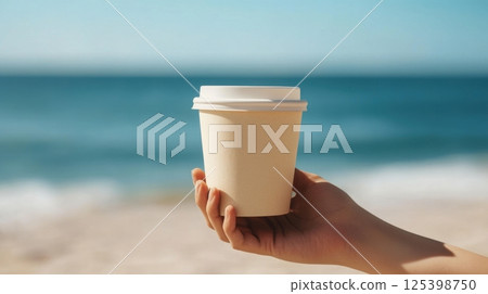 A hand holds a light beige takeaway coffee cup against a serene ocean backdrop, with soft waves and a clear blue sky A hand holds a light beige takeaway coffee cup against a serene ocean backdrop, with soft waves and a clear blue sky 125398750
