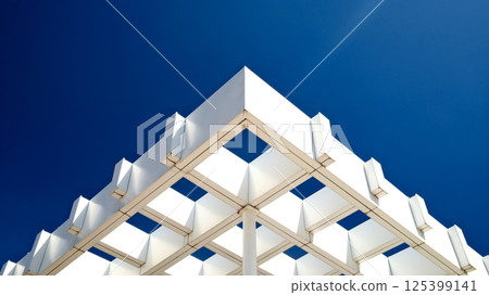 Striking modern architecture with geometric white pergola structure against deep blue sky 125399141