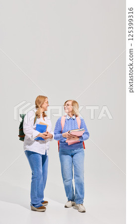 Full-length of two senior women with backpacks and books walking and talking giant white background. Elderly students. Full-length of two senior women with backpacks and books walking and talking giant white background. Elderly students. 125399316