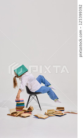 Elderly woman sitting on chair with book covering head, surrounded by many multicolored book against white background. 125399392