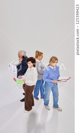 View from above on four elderly people, students involved in learning session, standing with books, studying against white background. View from above on four elderly people, students involved in learning session, standing with books, studying against white background. 125399423