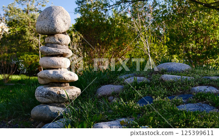 Zen garden meditation space with carefully balanced stone cairn, natural rock formations, lush green grass 125399611