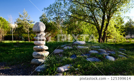 Zen garden meditation space with carefully balanced stone cairn, natural rock formations, lush green grass Zen garden meditation space with carefully balanced stone cairn, natural rock formations, lush green grass 125399614
