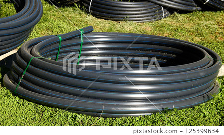 coiled black polyethylene irrigation pipes bundled with plastic ties on grassy construction site coiled black polyethylene irrigation pipes bundled with plastic ties on grassy construction site 125399634