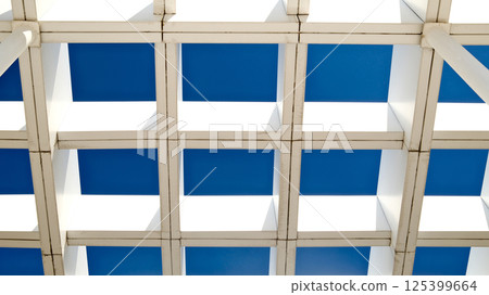 Striking modern architecture with geometric white pergola structure against deep blue sky Striking modern architecture with geometric white pergola structure against deep blue sky 125399664