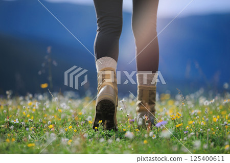 Hiker legs in leather boots walking on beautiful flowering grassland Hiker legs in leather boots walking on beautiful flowering grassland 125400611