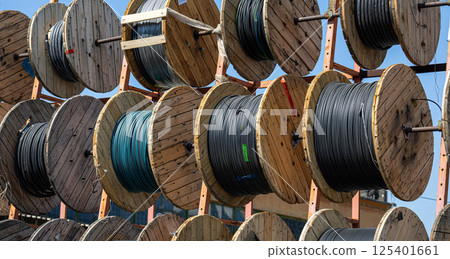 Multiple industrial cable reels stored outdoors, sunlight. Wooden spools are arranged in neat rows. Multiple industrial cable reels stored outdoors, sunlight. Wooden spools are arranged in neat rows. 125401661
