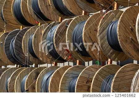 Tghtly packed wooden reels filled with heavy duty black cable at outdoor industrial depot. 125401662