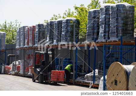 An outdoor industrial warehouse with large stacks of cable spools organized on metal shelves. 125401663