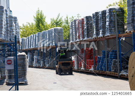 Industrial warehouse with stacked cable drums and coiled wires stored outdoors under sunlight. Industrial warehouse with stacked cable drums and coiled wires stored outdoors under sunlight. 125401665