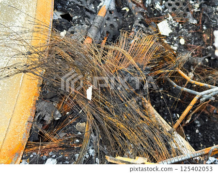 Burned car wiring harness with melted insulation and exposed copper strands, lying among charred debris and structural remains after intense fire damage 125402053