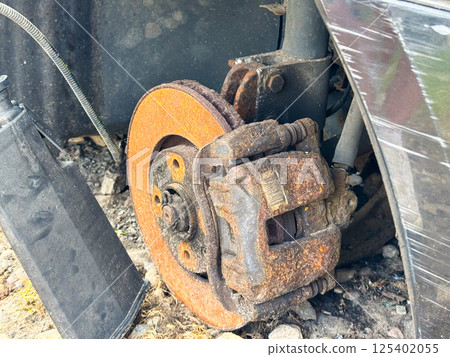 Rusted brake caliper and disc from a car showing severe corrosion on the braking system, with exposed suspension components and wheel hub assembly 125402055
