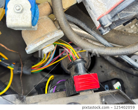 Close-up of a car engine wiring connector with red locking tab and multicolored wires, part of the vehicle's electrical harness located in the engine compartment Close-up of a car engine wiring connector with red locking tab and multicolored wires, part of the vehicle's electrical harness located in the engine compartment 125402059