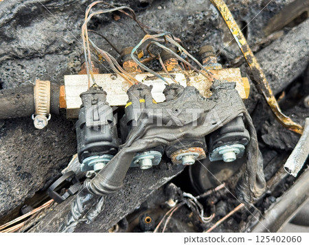 Burned fuel injector rail with connectors from a car engine, showing melted wiring insulation, scorched injectors, and heat-damaged fuel delivery system components 125402060