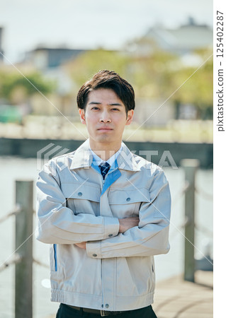 A young man in his 20s wearing work clothes with his arms crossed 125402287
