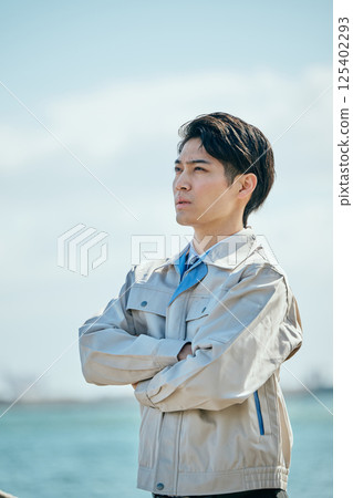 A young man in his 20s wearing work clothes gazing into the distance 125402293