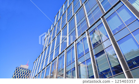 Modern office building with glass facade on a clear sky background. Transparent glass wall of office building. Modern office building with glass facade on a clear sky background. Transparent glass wall of office building. 125403357