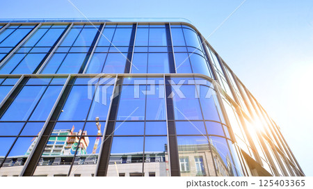 Modern office building with glass facade on a clear sky background. Transparent glass wall of office building. Modern office building with glass facade on a clear sky background. Transparent glass wall of office building. 125403365