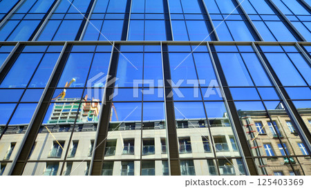 Modern office building with glass facade on a clear sky background. Transparent glass wall of office building. Modern office building with glass facade on a clear sky background. Transparent glass wall of office building. 125403369
