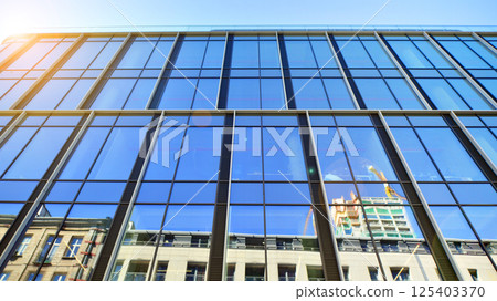 Modern office building with glass facade on a clear sky background. Transparent glass wall of office building. Modern office building with glass facade on a clear sky background. Transparent glass wall of office building. 125403370