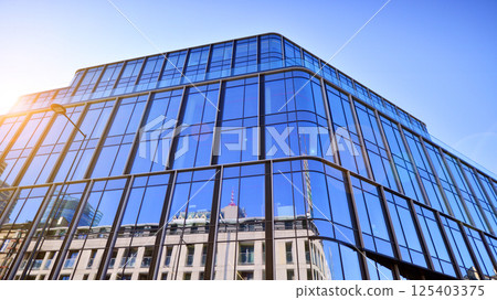 Modern office building with glass facade on a clear sky background. Transparent glass wall of office building. Modern office building with glass facade on a clear sky background. Transparent glass wall of office building. 125403375