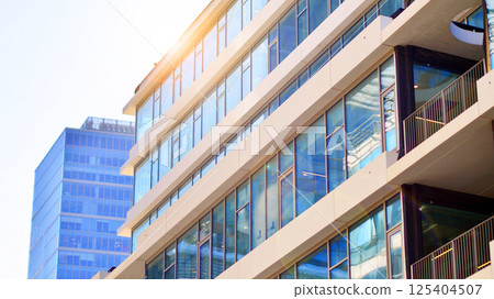 Downtown corporate business district architecture. Glass reflective office buildings against blue sky and sun light. Economy, finances, business activity concept. Rising sun on the horizon. 125404507