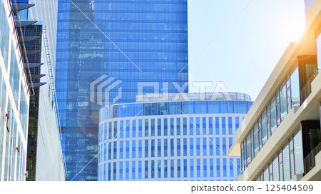 Downtown corporate business district architecture. Glass reflective office buildings against blue sky and sun light. Economy, finances, business activity concept. Rising sun on the horizon. Downtown corporate business district architecture. Glass reflective office buildings against blue sky and sun light. Economy, finances, business activity concept. Rising sun on the horizon. 125404509