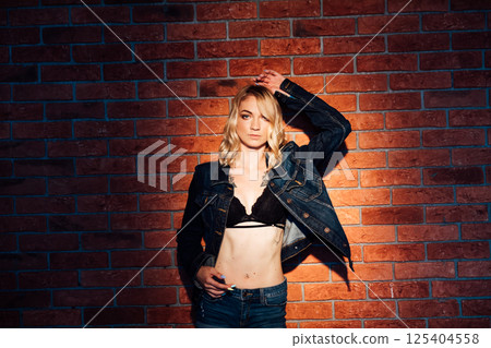 woman in jacket and lingerie standing against brick wall 125404558