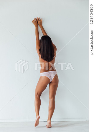 Brunette in lingerie stands with her back to a white wall 125404599