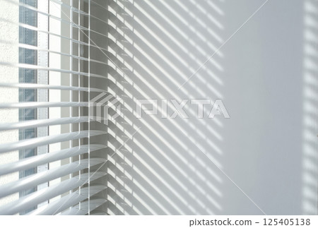 Sunlight casting striped shadows through white window blinds onto a clean wall 125405138