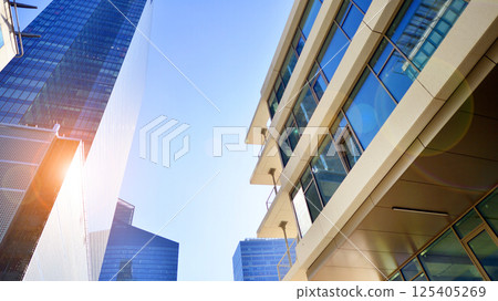 Downtown corporate business district architecture. Glass reflective office buildings against blue sky and sun light. Economy, finances, business activity concept. Rising sun on the horizon. 125405269
