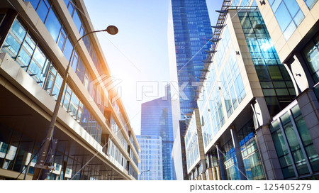 Downtown corporate business district architecture. Glass reflective office buildings against blue sky and sun light. Economy, finances, business activity concept. Rising sun on the horizon. 125405279