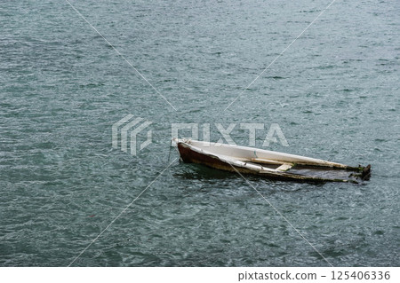 close up of a small, weathered boat gently floating on calm water, partially submerged in the sea with copy space 125406336