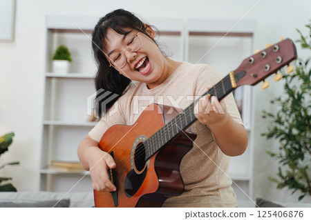 Happy Asian women play acoustic guitar and singing on the sofa in living room at home 125406876