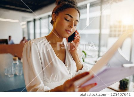 A woman is engaged on the phone while reviewing important documents in a modern office space 125407641