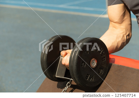 Athlete muscular man practicing with black dumbbell at outside gym. Close up. for workout. 125407714