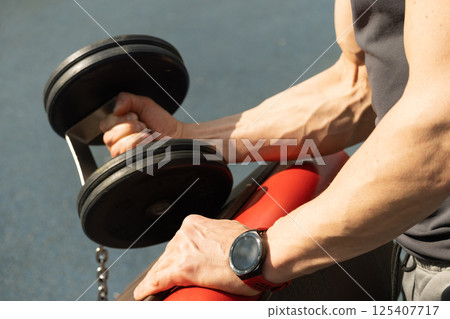 Athlete muscular hand with black dumbbell at outside gym. Close up. 125407717