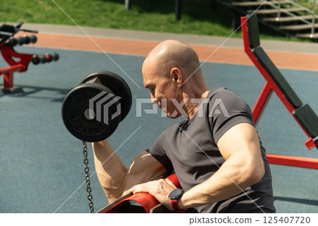 Athlete muscular man practicing with black dumbbell at outside gym. Open air gym and workout. Close up. 125407720