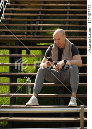 Sporty man relax, sitting on stairs using phone and texting social media after training. Summer healthy leisure activity. Outdoors. Sporty man relax, sitting on stairs using phone and texting social media after training. Summer healthy leisure activity. Outdoors. 125407721