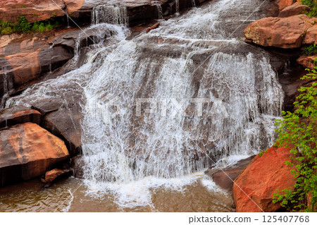 Fresh waterfall flows over rocky surface, creating serene atmosphere surrounded by greenery rugged terrain. Fresh waterfall flows over rocky surface, creating serene atmosphere surrounded by greenery rugged terrain. 125407768