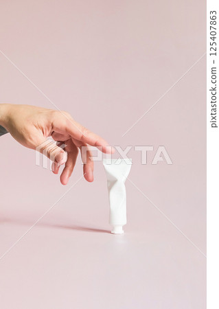 Females Hand Reaches Towards Small Crumpled White Cosmetic Product Tube. Beauty Treatment Concept. 125407863