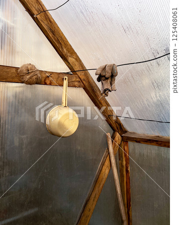 Wooden beams in a greenhouse, displaying hanging mittens, a ladle, and twine, rustic, utilitarian scene, highlighting simple gardening tools for everyday use 125408061