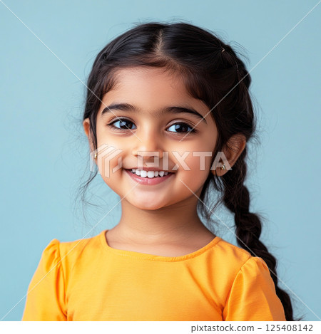 A cheerful, young Hindu girl, smiling happily in front of a plain pastel background, captured in a commercial style, showcasing innocence and joy, great for advertising campaigns 125408142