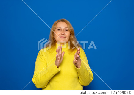 Caucasian woman in her 40s feeling happy and successful, smiling and clapping, saying congratulations with a handclap against a blue wall. Caucasian woman in her 40s feeling happy and successful, smiling and clapping, saying congratulations with a handclap against a blue wall. 125409038