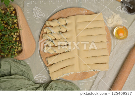 Top view twisted dough strips on wooden board. Cutter, egg, green towel, microgreens sprouts on kitchen table. Home cooking baking puffs Top view twisted dough strips on wooden board. Cutter, egg, green towel, microgreens sprouts on kitchen table. Home cooking baking puffs 125409557