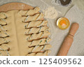 Top view close up twisted dough strips on wooden board. Cutter, egg, rolling pin on kitchen table. Home cooking baking puffs 125409562