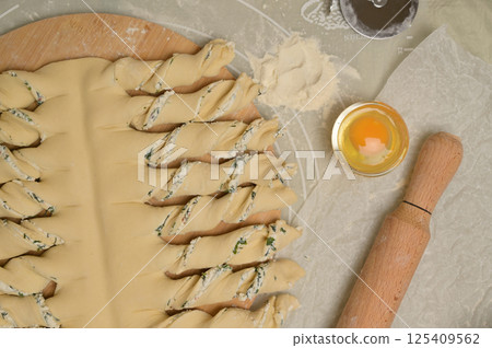 Top view close up twisted dough strips on wooden board. Cutter, egg, rolling pin on kitchen table. Home cooking baking puffs 125409562