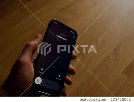 Fraud or fraudulent schemes. Close-up of a male hand holding a phone with an unexpected incoming call from an unknown 125410002