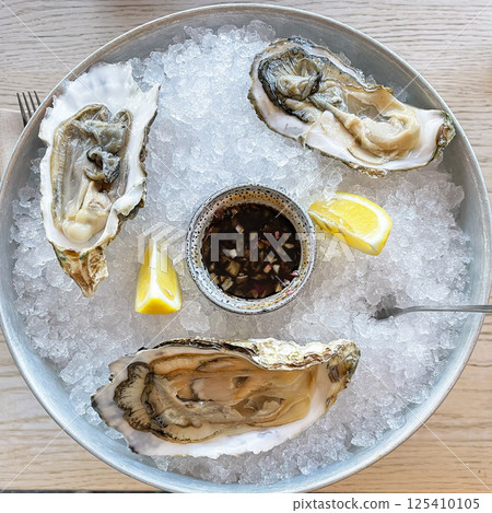 Open oysters on a vintage vintage dish with slices of crushed ice and half a lemon closeup on a black stone textured background. Right angle view from above. Aphrodisiac. Open oysters on a vintage vintage dish with slices of crushed ice and half a lemon closeup on a black stone textured background. Right angle view from above. Aphrodisiac. 125410105